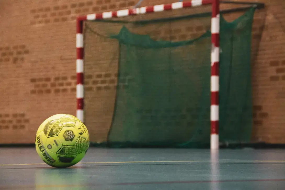 un ballon placé au sol dans une salle sportive, devant un goal